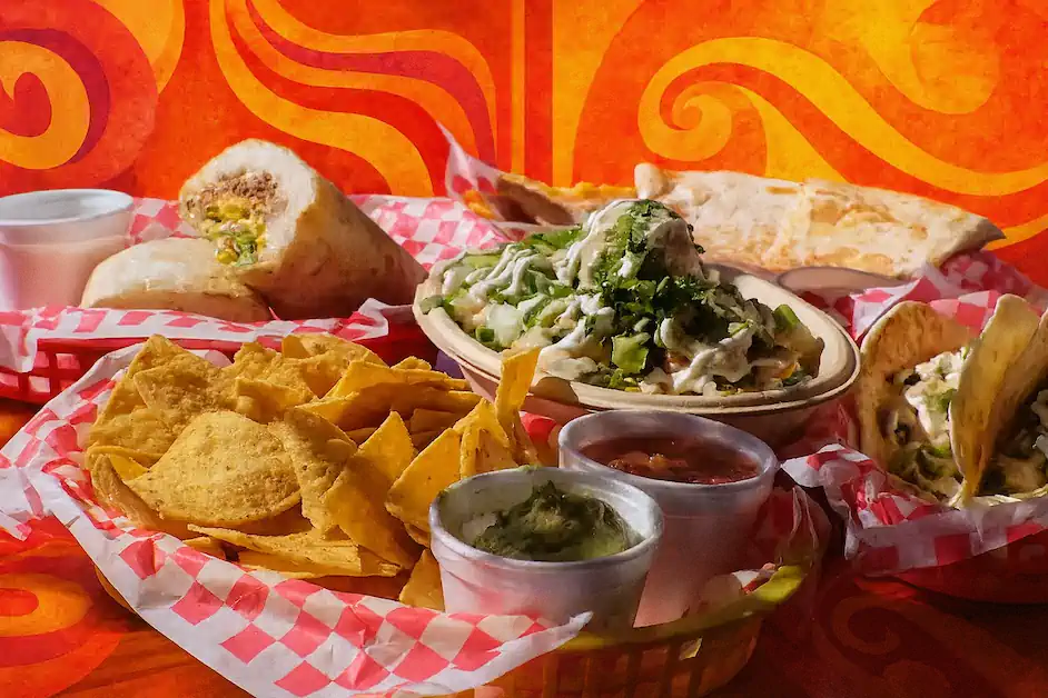 A Rock the Guac spread — basket of tortilla chips, hand-smashed guac and salsa, tacos, a loaded burrito and a quesadilla on red-check paper